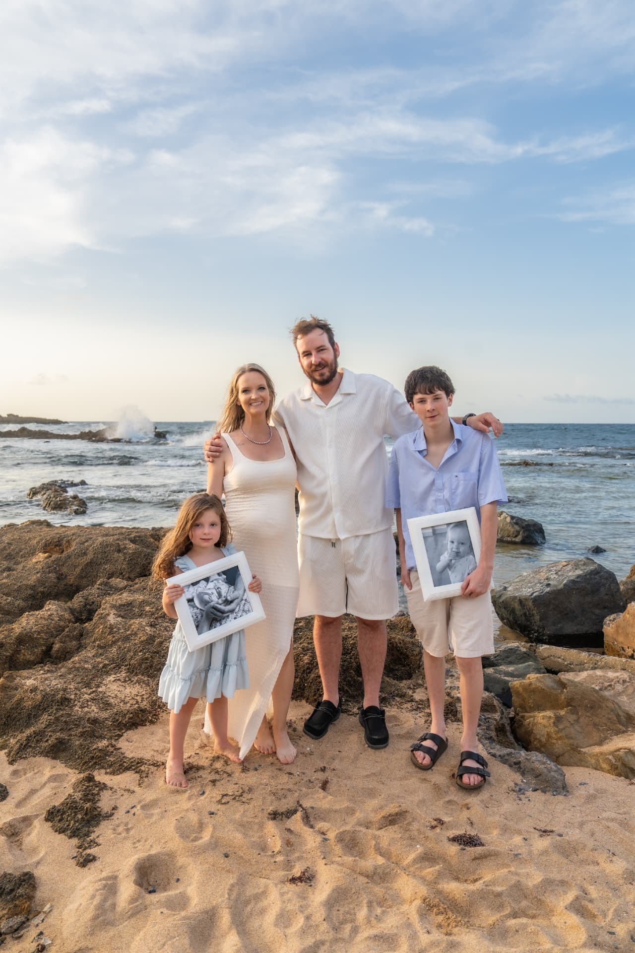 The Eggleston family on a rocky shoreline, holding framed photographs of Caia and Cambrie in remembrance.